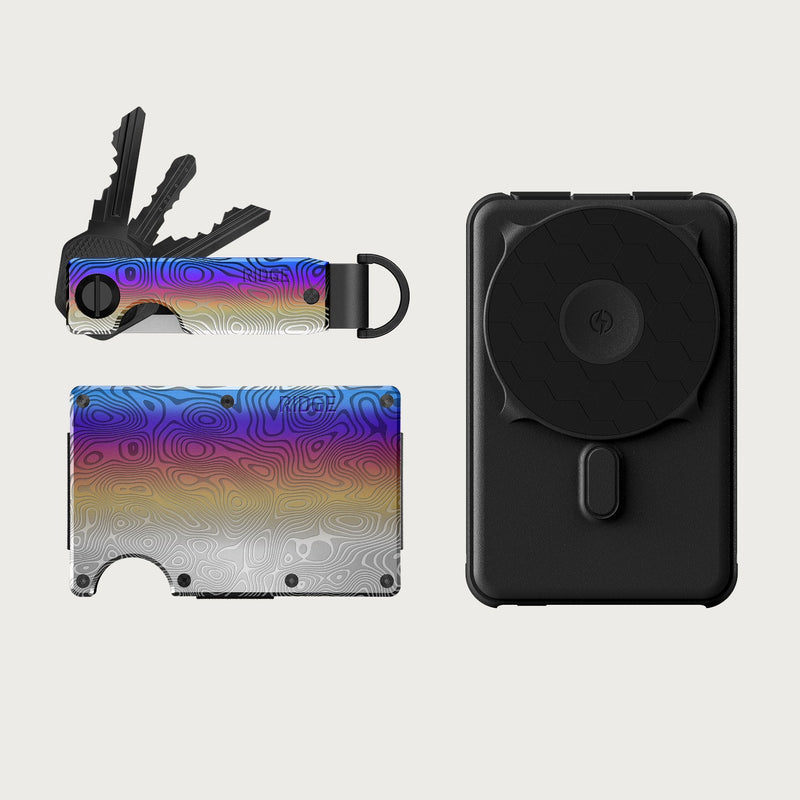 Ridge Wallet + Power Bank + KeyCase - Burnt Damascus: wallet and keycase in rainbow topographic finish, keys attached, black power bank with wireless charging disc.